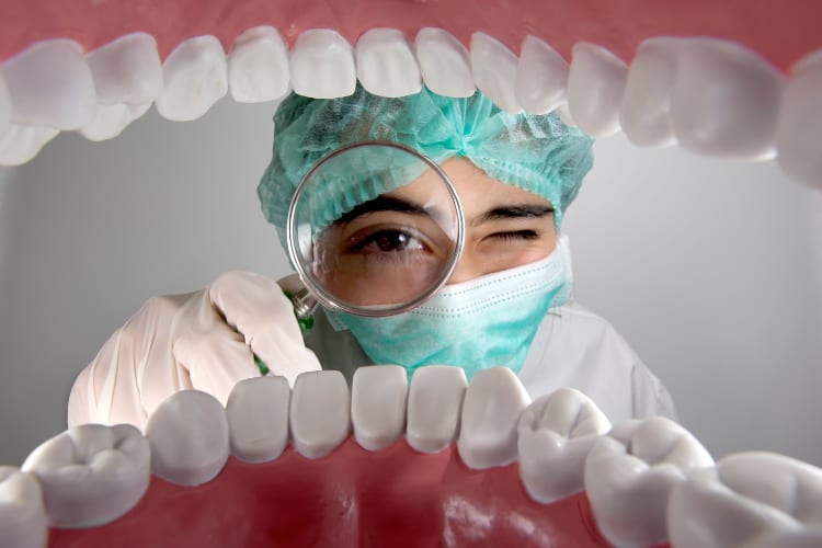 Odontólogo con lupa revisando la boca durante una consulta de prevención